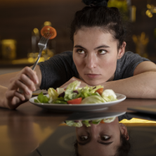 Mujer joven mirando su comida, indecisa debido a problemas emocionales relacionados con la alimentación.