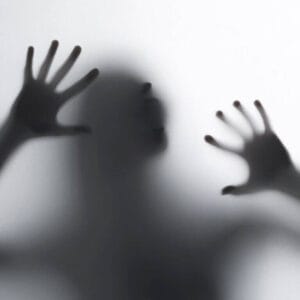 Silueta en blanco y negro de mujer atrapada por el miedo, gritando tras un cristal esmerilado.